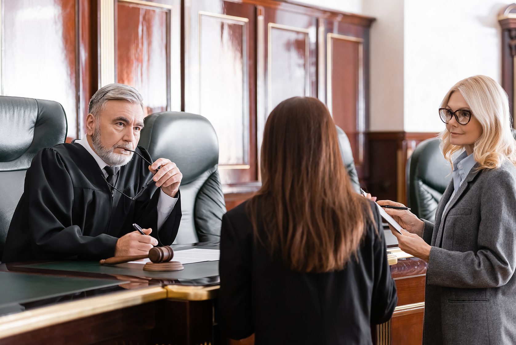 thoughtful judge holding eyeglasses listen to prosecutor standing near attorney in court Thoughtful Judge Holding a Hearing